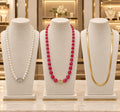 Description: Three elegant necklaces displayed separately on premium cream velvet stands in a luxurious jewelry showroom. Featuring a pearl necklace, a beautiful pink bead necklace, and a golden chain. High-definition quality,